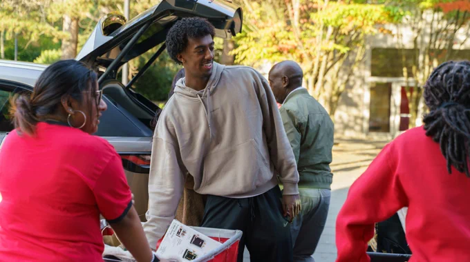 Group of people unpacking items from a car trunk on a sunny day on the Seattle University campus.
