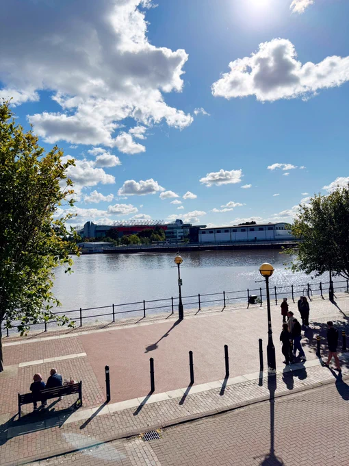 A photo of Old Trafford over the water from Salford Quays. The sun is shining.