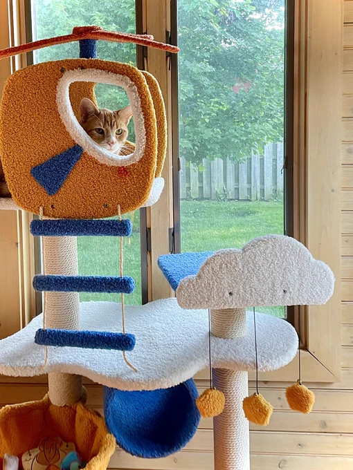 an orange boy cat sits perched in the helicopter pedestal of his play tower