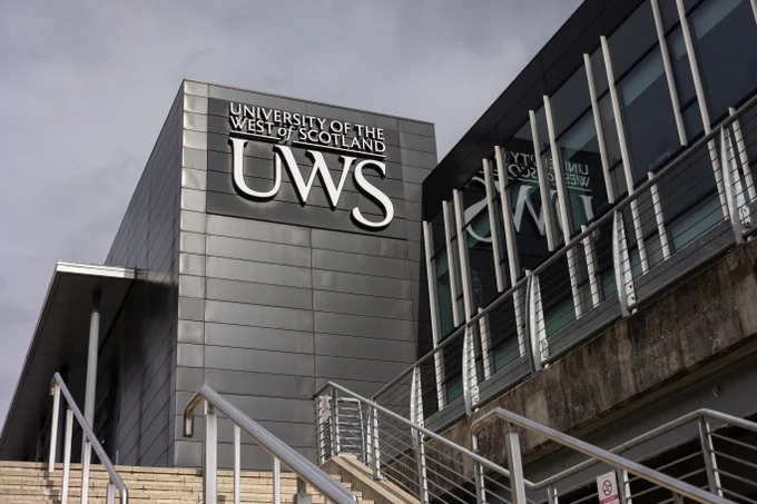 Exterior view of the University of the West of Scotland building with the initials UWS prominently displayed on the facade under a cloudy sky.