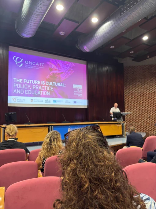 An auditorium full of people. One person presents on a stage with a large screen behind. Encatc conference 2025