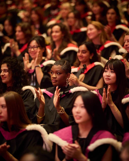 Graduates in traditional academic regalia clap during a graduation ceremony.