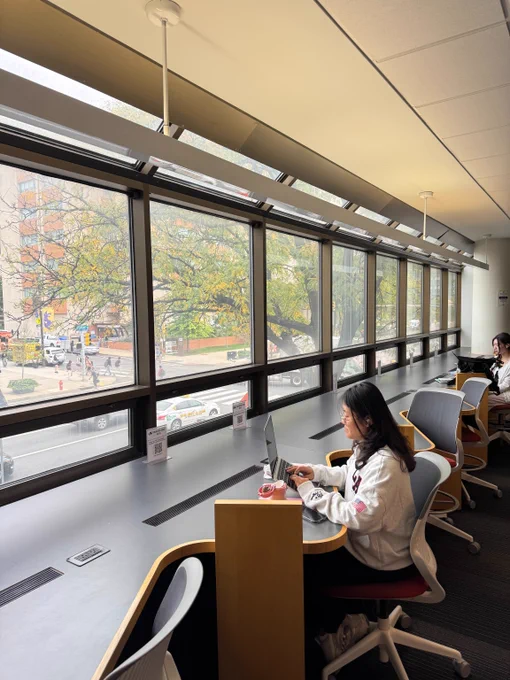 Students studying with fall foliage in window background, on Drexel's campus with students passing on Market st. 
