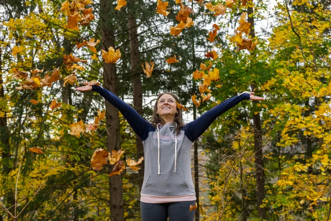 woman in a hoodie throws leaves into the air