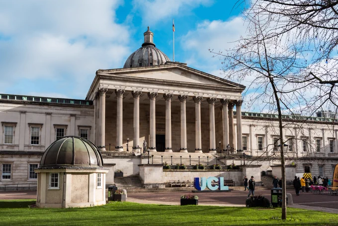 View of the UCL (University College London) main building with a large dome and columns in front, under a clear sky. People are visible sitting and walking in the foreground.