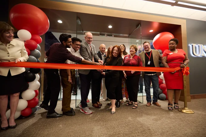 Group of individuals participating in a ribbon-cutting ceremony at UNLV, surrounded by red and black balloons.
