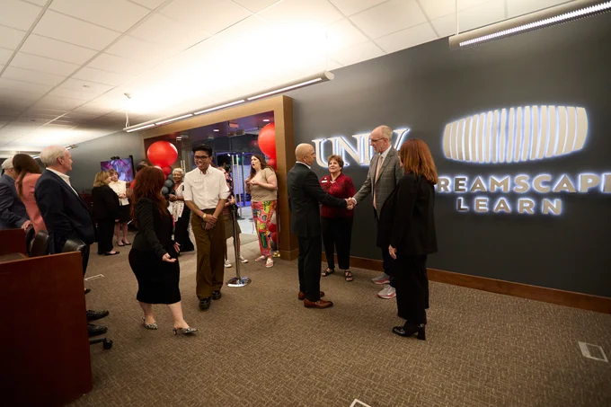 Group of people mingling in a room with "UNLV DREAMSCAPE LEARN" written on the wall.
