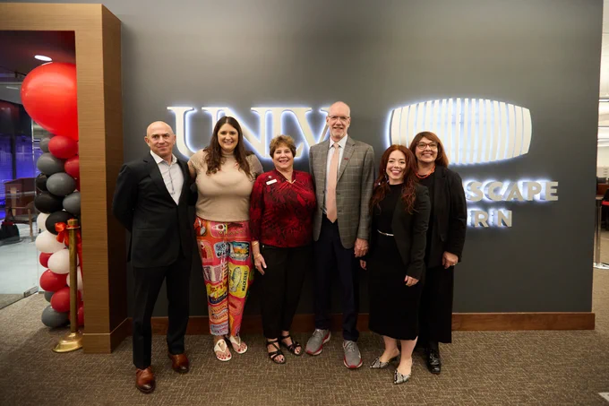 Five individuals posing in front of a lit 'UNLV' sign and 'DREAMSCAPE ROOM' text at a grand opening event for an extended reality space