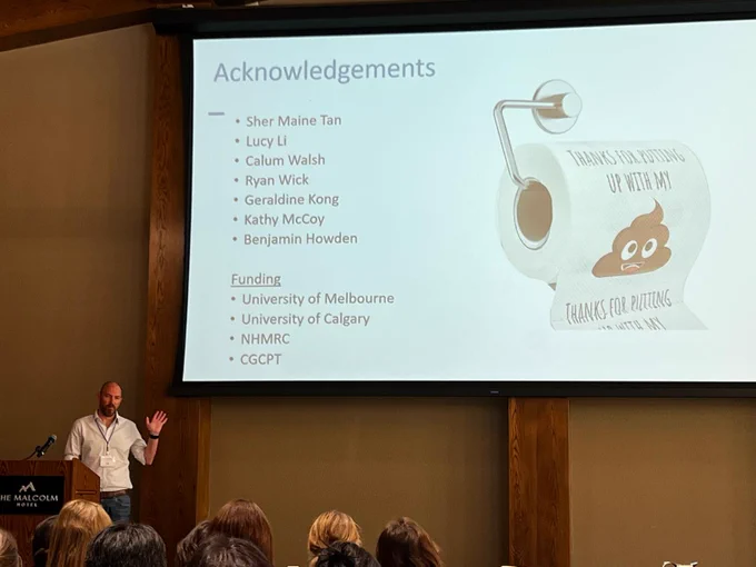 A man waving at a lectern in front of an acknowledgements slide.