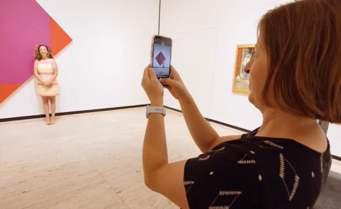 A woman is taking a photo of another woman in front of one of the Go Big Red exhibit pieces.
