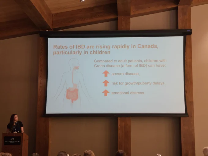 A white woman presenting a slide that reads: Rates of IBD are rising rapidly in Canada, particularly in children. Compared to adult patients, children with Crohn disease (a form of IBD) can have: increased incidence of severe disease, increased risk for growth/puberty delays, and increased emotional distress.