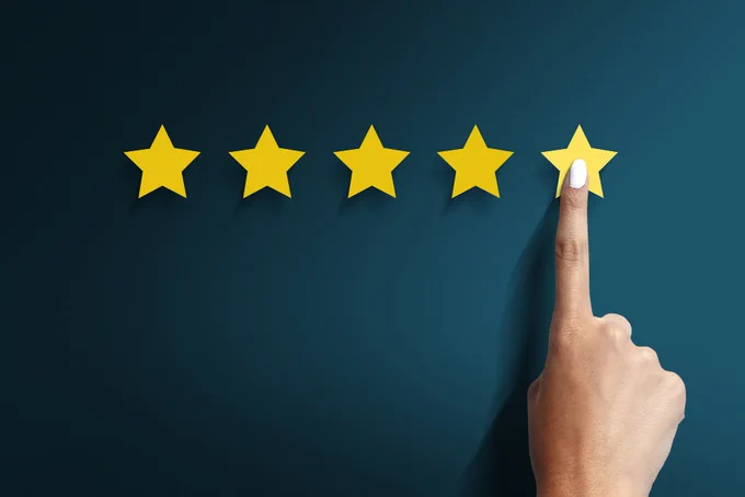 A hand with a pointed finger hovering over a row of five yellow stars against a dark background, indicating a rating or review system.