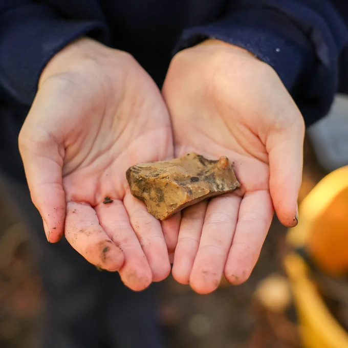 Image shows a pair of hands holding an artefact that was found during the dig.
