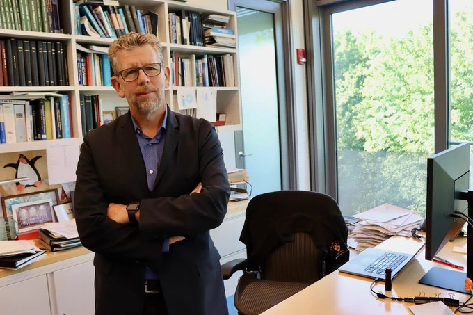 Full-color image of PI standing in his office, window in background.