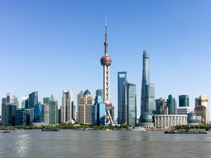 Shanghai skyline on the water under a blue sky.