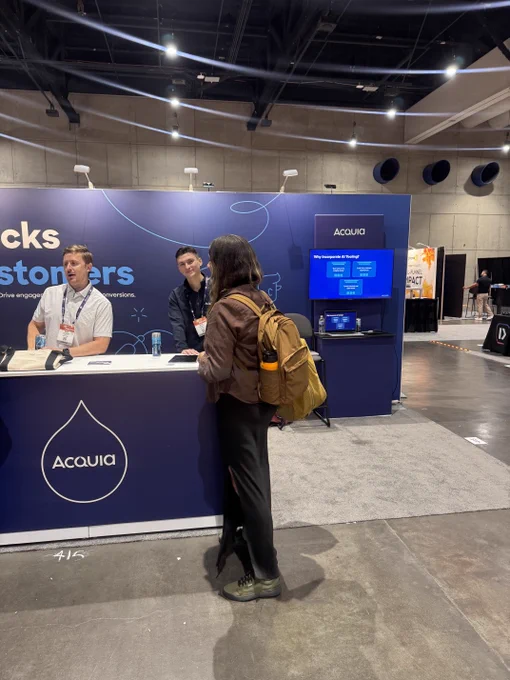 Person with a yellow backpack engaging with two representatives at the Acquia booth during a Content Marketing World Conference.
