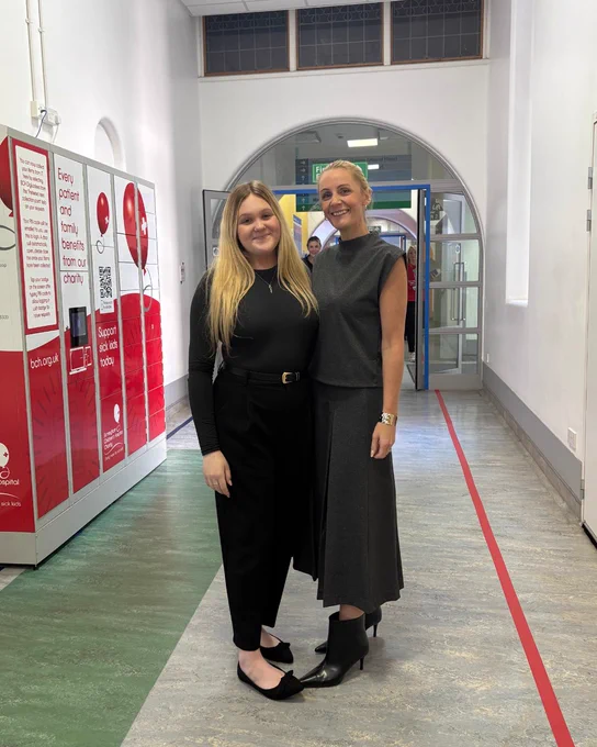 Ellen and Kirsty stood in a hospital corridor smiling at the camera.