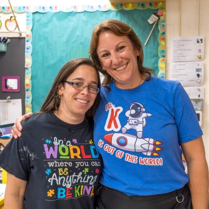 Two Marlborough ECC teachers stand, smiling and side by side, looking directly at the camera.