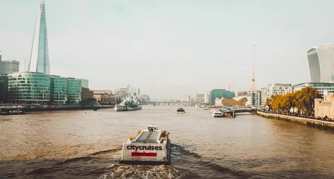 View of the River Thames featuring a City Cruises boat, with the Shard and the Walkie Talkie building visible in the background.