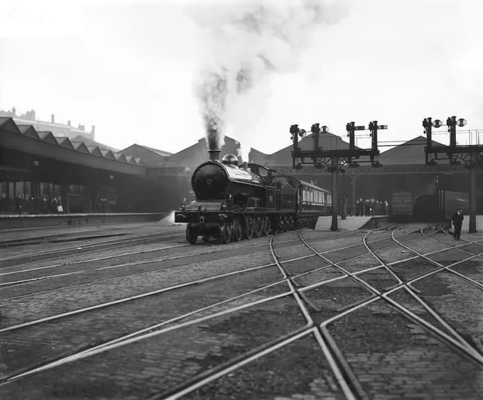 Photograph from 1909, showing a steam engine leaving Euston station, passing a signal gantry with a plume of smoke emerging from the funnel. Courtesy National Railway Museum.