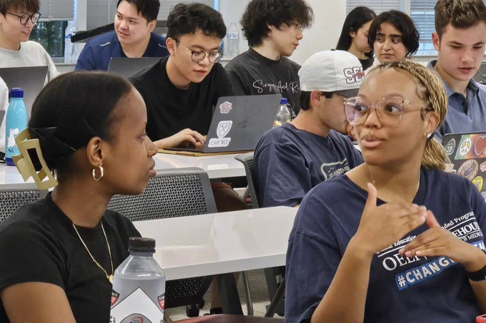 Students sitting at desks engaged in a discussion during AI.Xperience. 