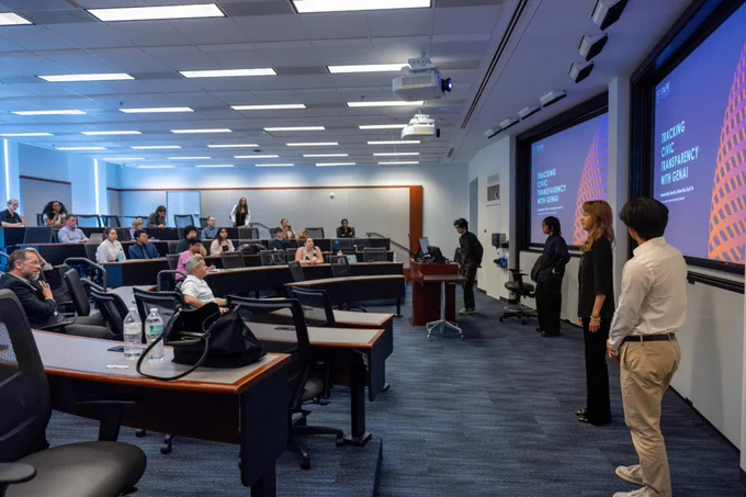 Students presenting in a lecture hall during AI.Xperience, with two large projection screens in the back.