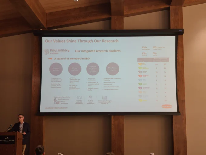 An image of a man standing at a lectern presenting a slide showing an overview of his company's research portfolio.