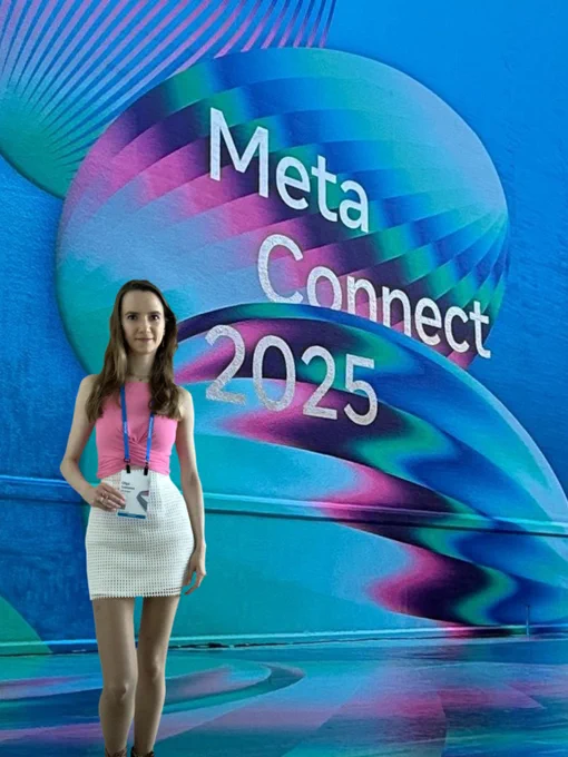Olga, the founder of VR Oxygen, is standing in front of the wall painted with a Meta Connect 2025 logo and holding her badge in her right hand.