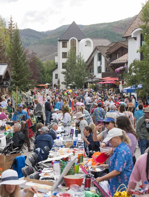 A bustling outdoor event in Vail with many people at tables along a street, surrounded by mountainous scenery and European-style architecture.