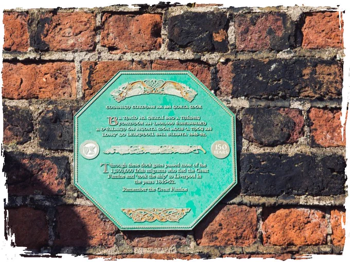 A green, octagonal historical marker plaque mounted on a red brick wall, commemorating the 150th anniversary of the Great Famine.