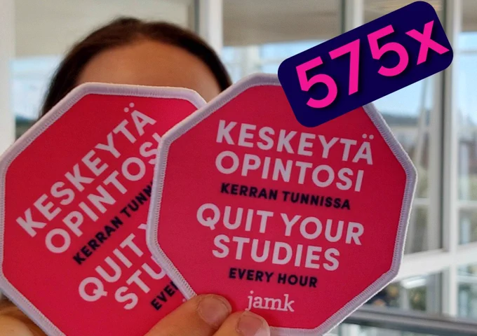 Henkilöllä on kädessä kaksi haalarimerkkiä.
