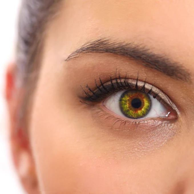 Close-up of a woman's eye with striking green and amber hues and long, dark eyelashes.