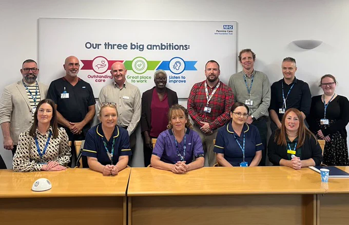 Thirteen health and care colleagues sitting in a boardroom, with a 'three big ambitions' sign in the background.