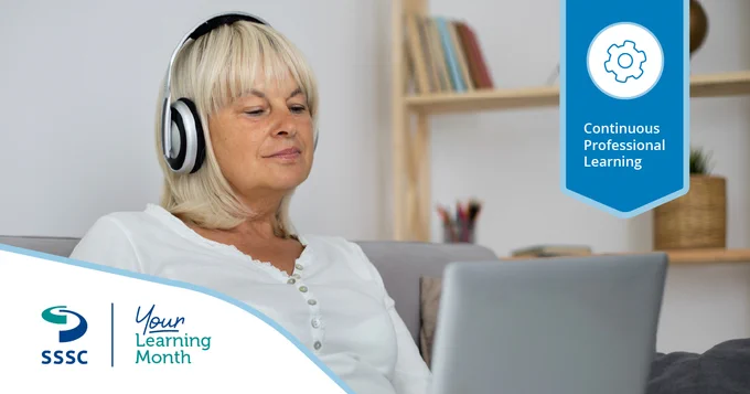 Woman wearing headphones sitting on a couch using a laptop for online learning in a cozy room with bookshelves.