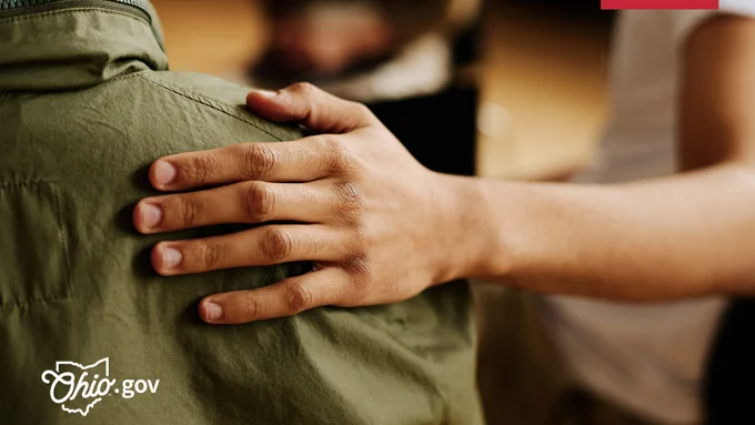 A woman places a reassuring hand on a man’s shoulder.
