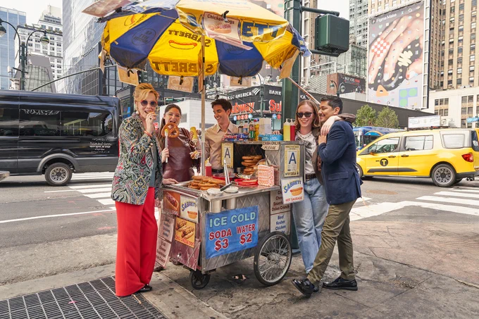 Hacks cast posing by a hotdog cart in New York City. Left to right: Jean Smart, Megan Stalter, Paul W. Downs, Hannah Einbinder, Mark Indelicato.