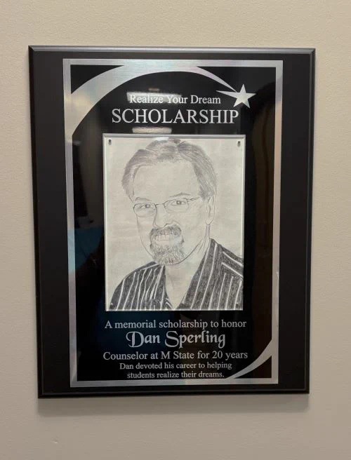 Memorial scholarship plaque for Dan Sperling, featuring a black and white portrait and text detailing his 20 years as a counselor at M State, dedicated to helping students achieve their dreams.