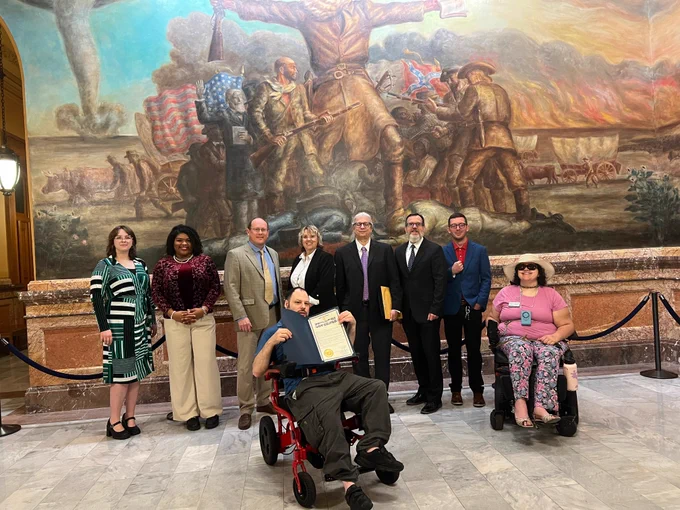 Photo of group of disability advocates in front of the John Brown Mural at the Capitol.