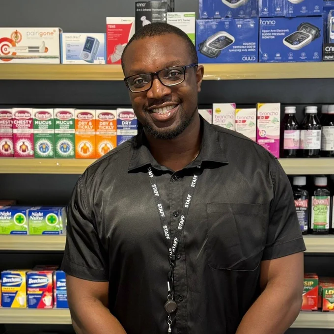 Damisola is smiling in front of medicine shelves in a community pharmacy