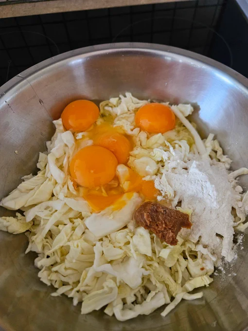 Okonomiyaki ingredients in a mixing bowl of shredded cabbage, four cracked eggs, a tablespoon of flour, a teaspoon of miso.