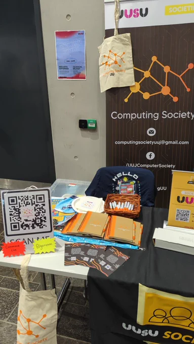 A photo of our UU Computing stall at the Freshers Fayre. There is a QR code sign up, as well as pens and notebooks.