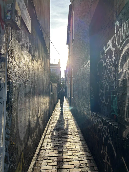 Photo of a person in the laines brighton – the sun is shining and their shadow can be seen in forground on cobbled streets 