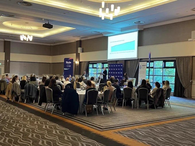 A filled room with large round tables and a projector showing a graph overhead.