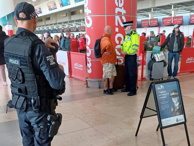 Project Servator officer speaking to a passenger at a deployment in Liverpool John Lennon Airport, supported by officers from Armed Policing