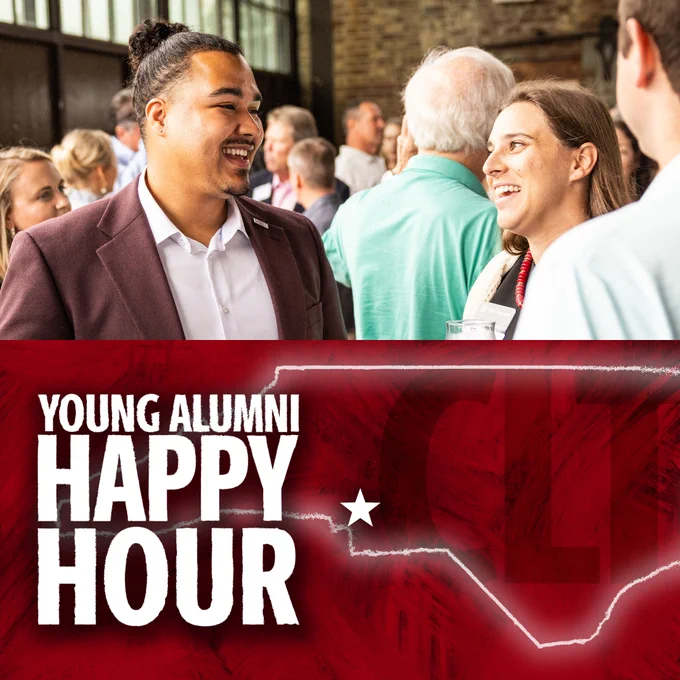 Two individuals smiling and conversing at a 'Young Alumni Happy Hour' event with other attendees in the background.