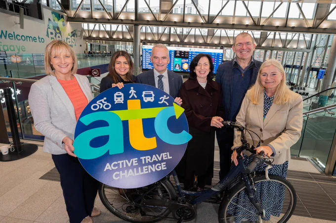 Group of 4 females and 2 males from Translink and participating organisations. 

Group is standing upstairs at Grand Central Station around a bicycle and holding a 'atc Active Travel Challenge' logo photo prop