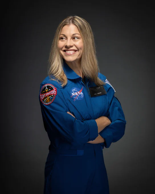 Astronaut Candidate Individual Official NASA Portraits - ASCAN Class of 2025 - Anna Menon seen in her blue flight suit with arms crossed looking to the left with her hair down and in front of a black to gray background. Photo credit: NASA/Bill Stafford