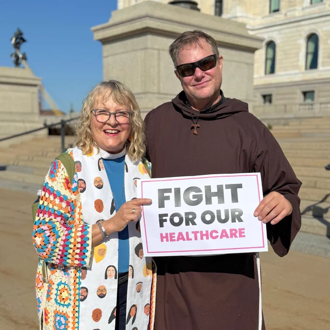 Photo shows two clergy members holding sign that says: "Fight for our healthcare"