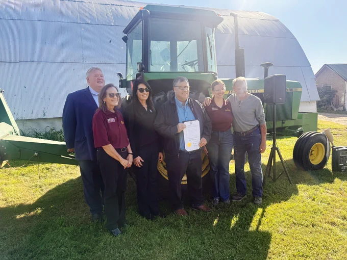 Sen. Rich Draheim, Rep. Bobbie Harder, MDA Commissioner Thom Petersen, Extension Dean Bev Durgan, Extension Farm Safety Educator Emily Krekelberg and Dale Krekelberg stand in front of a tractor on a farm.