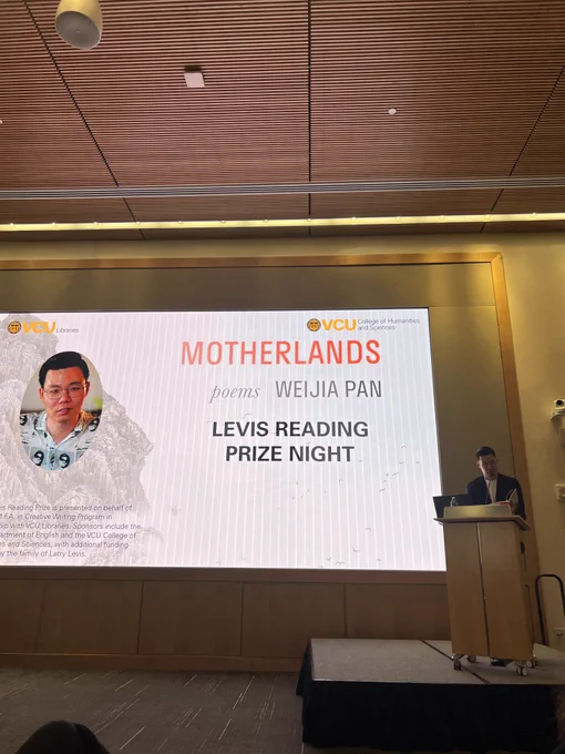 Weijia Pan reads from his collection at a podium on a stage. Behind him, a large screen reads: MOTHERLANDS: poems, Weijia Pan, Levis Reading Prize Night.